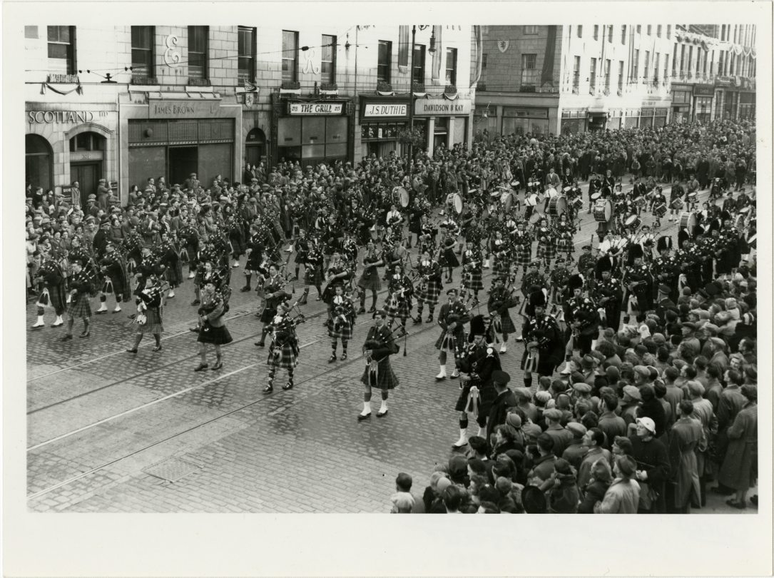 Pipers leading the coronation parade through Union Street with crowds of onlookers.