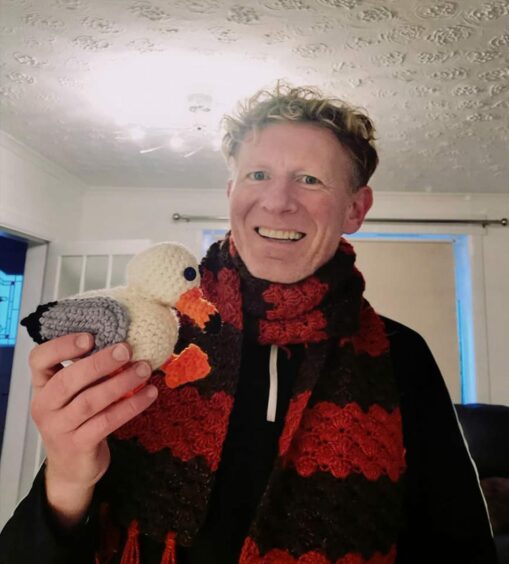 Gordon Morris holding a knitted scarf and seagull which were made by a fan of the series. Image: Supplied.