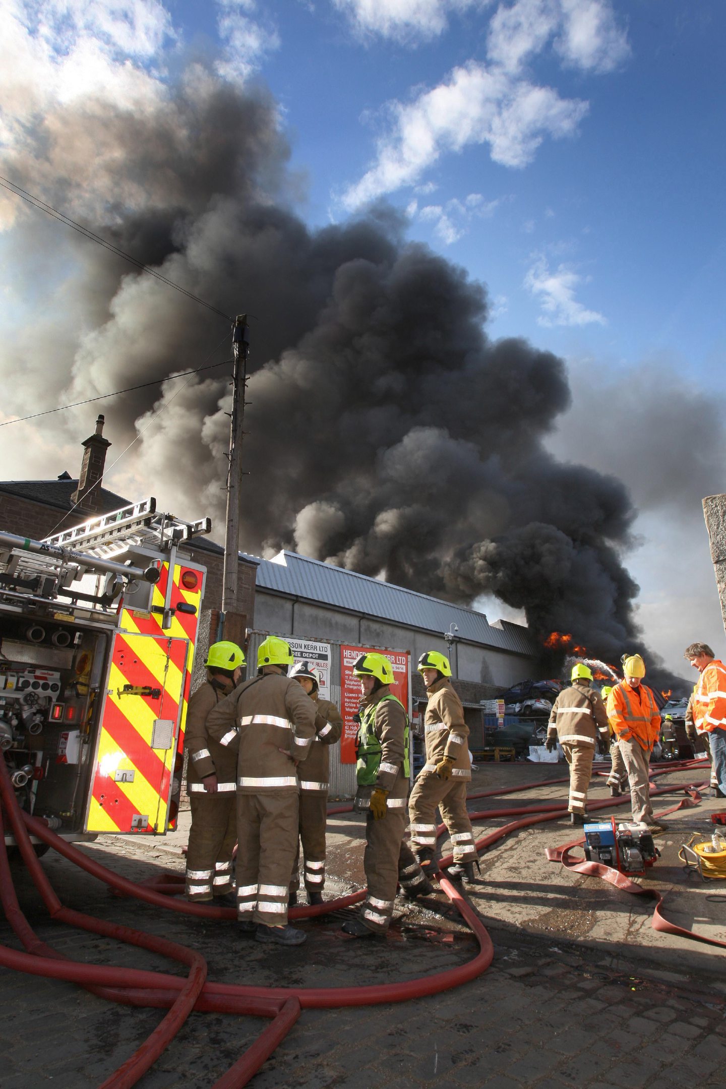 Fire crews on the scene as the pall of black smoke rises behind