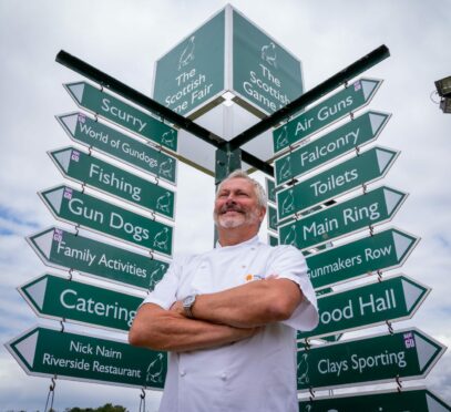 Nick Nairn in a chef's jacket standing in front of a large signpost at the Scottish Game Fair.