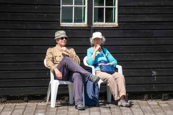 A couple sit on seats enjoying the sunny weather. 