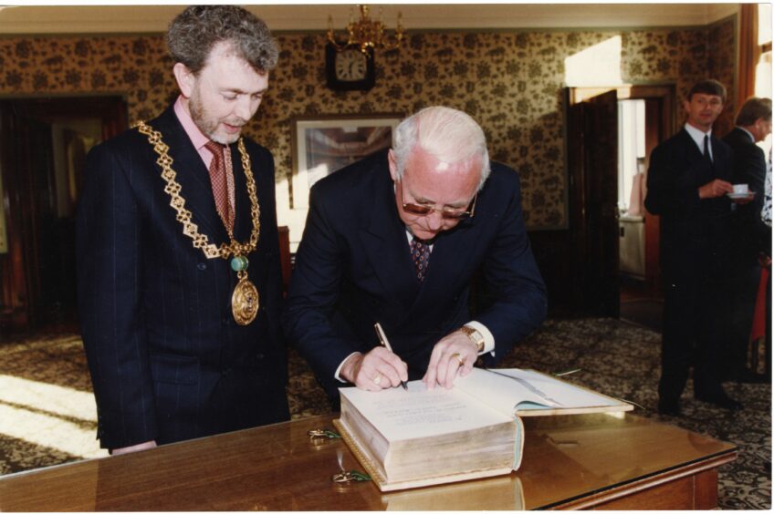 Jim McLean signs the book in the Caird Hall, watched by Lord Provost Tom McDonald. Image: DC Thomson.