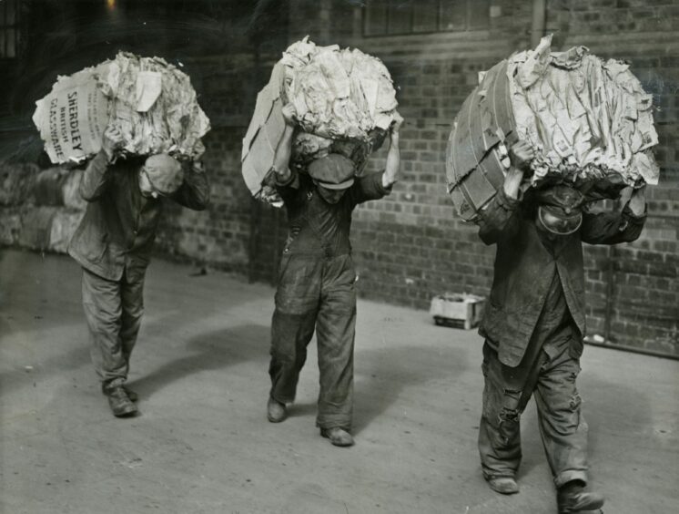 Three individuals carrying large bales of paper on their backs. Image: DC Thomson.