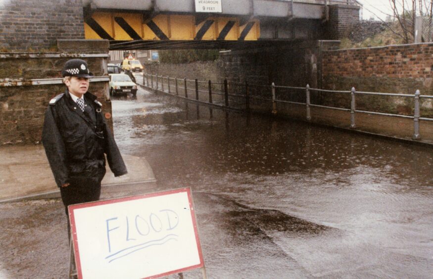 Cars attempting to drive through the floodwater, as a PC looks on. Image: DC Thomson.