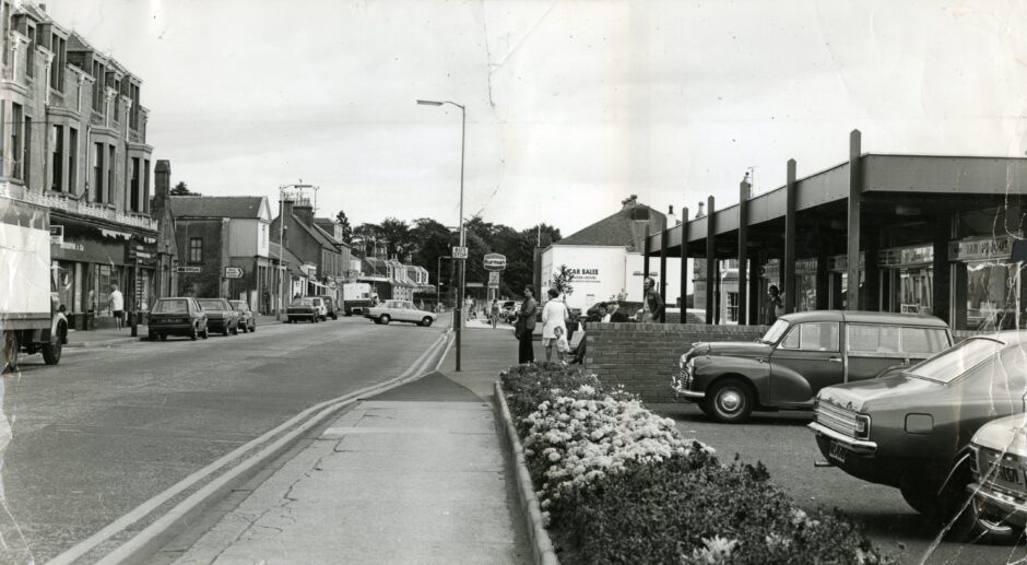 There are shops and cars on either side of the street in this image from 1976. Image: DC Thomson.