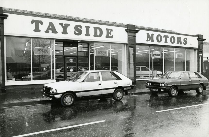 Two cars are parked outside and several cars are visible through the showroom window of Tayside Motors in Monifieth in March 1980.