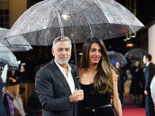 George and Amal Clooney bared the British storms as they took to the red carpet for a special screening of his new film The Boys In The Boat (Ian West/PA)