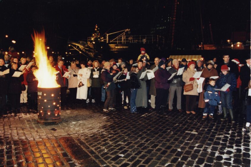 People gather around a brazier for the Christmas concert at RRS Discovery in 1999. 