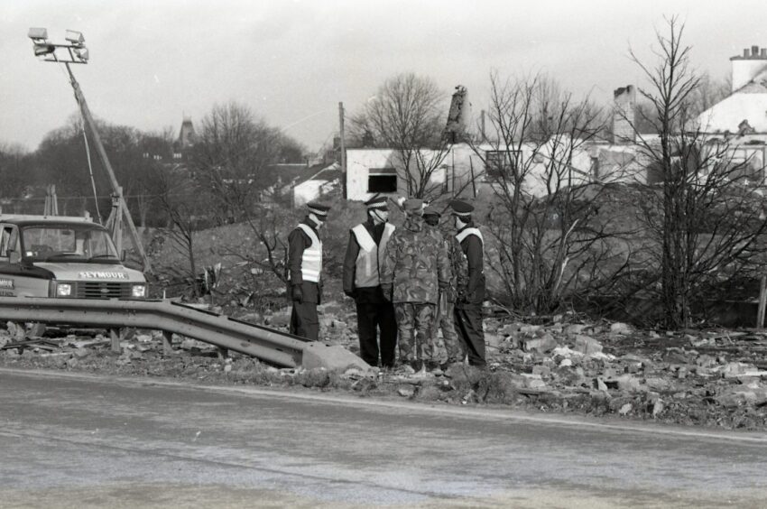 Emergency services workers stand amid debris by the side of a road