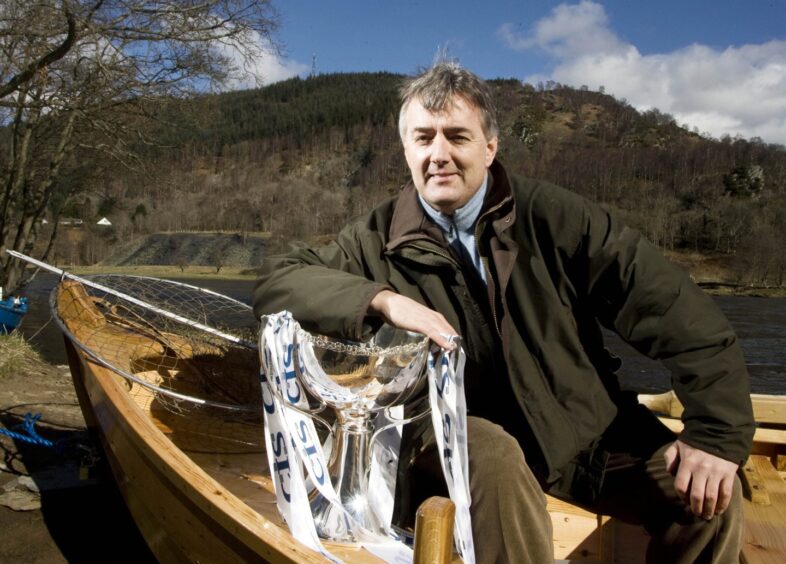 Redford poses lochside, in a small boat, with a trophy won later in his career