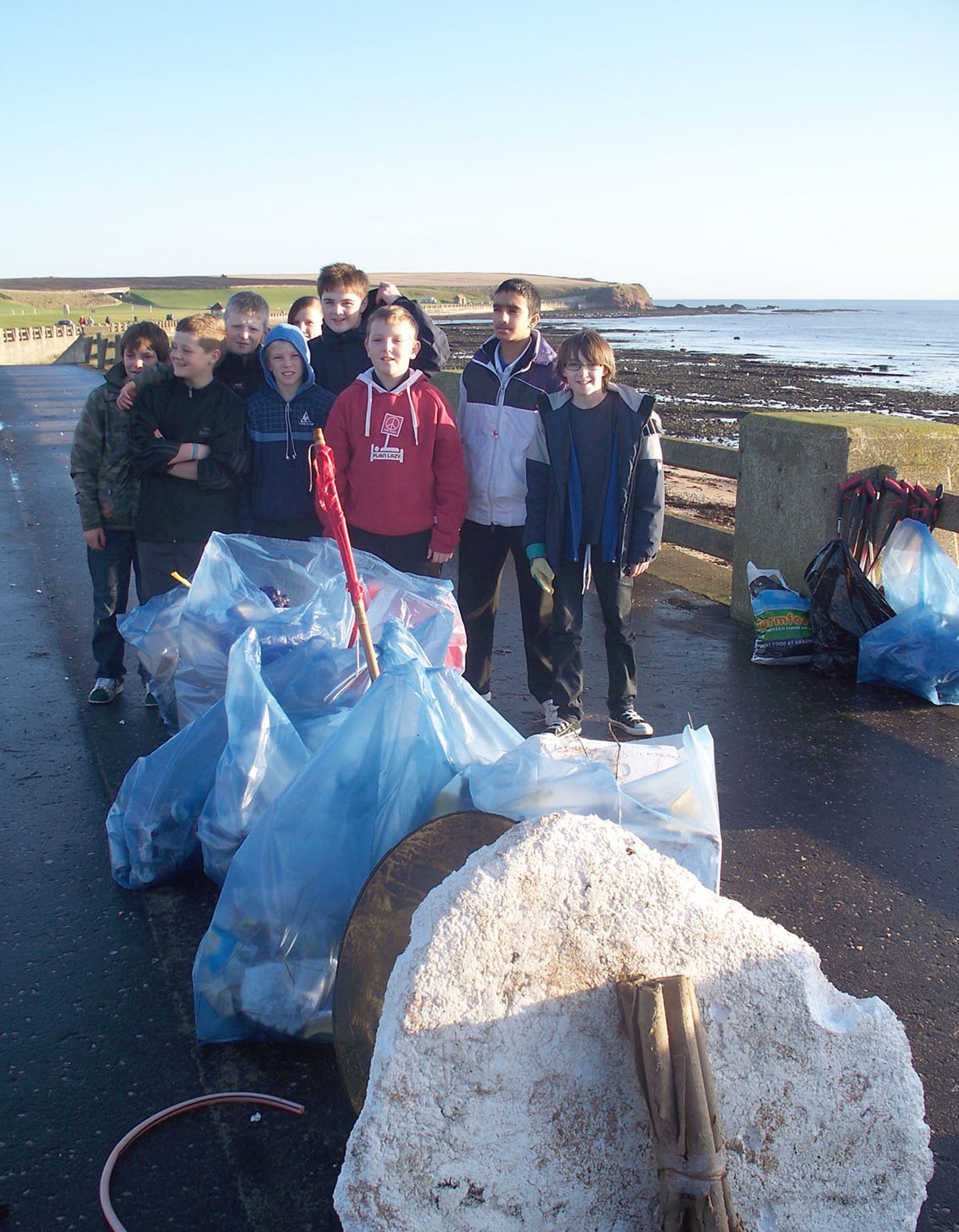 Pupils with bags of rubbish tidying up at Victoria Park, with the coastline in the background