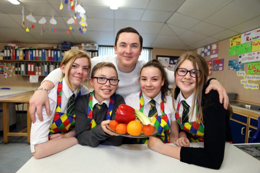 Dean Banks with home economics pupils, one holding a bowl of fruit, during his visit. 