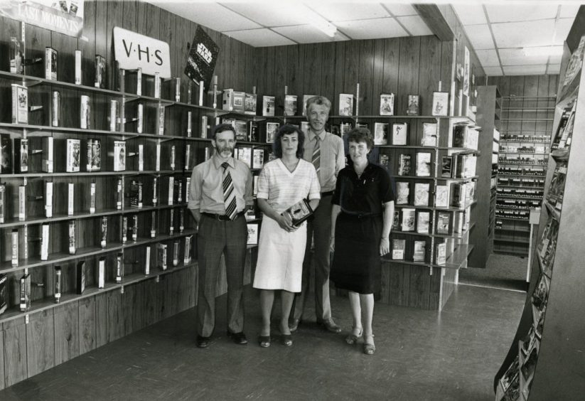 Staff inside the Cherry Video store in 1982, standing before a wall of tapes under a VHS sign