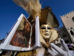 A man wears a mask and holds a replica of Marco Polo’s travelogue as part of the Venice carnival (AP Photo/Luca Bruno)