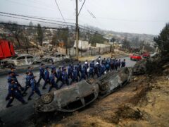 Navy personnel walk past overturned and charred cars as they deploy to help those affected by forest fires in Chile (Esteban Felix/AP)