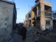 Palestinians walk by a residential building destroyed in an Israeli strike in Rafah (AP Photo/Hatem Ali)