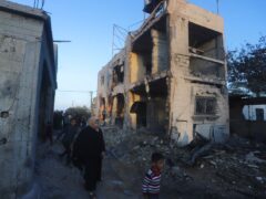 Palestinians walk by a residential building destroyed in an Israeli strike in Rafah on Sunday (Hatem Ali/AP)