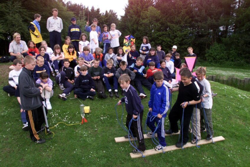 Pupils enjoying the day at Clatto, a large group watching four pupils trying to walk using two boards