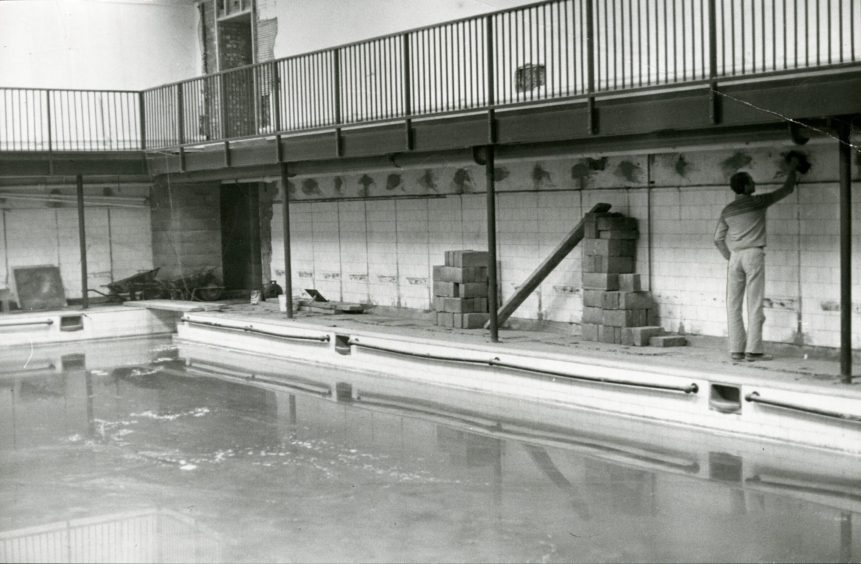 A man works on the tiles beside the pool at Lochee swimming baths.