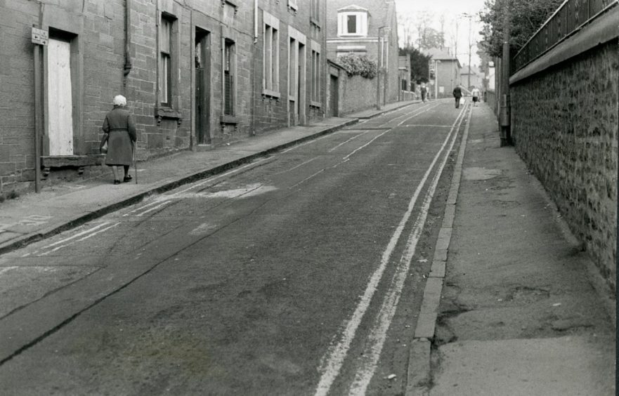 Two people walking on the narrow Bright Street in Lochee. 