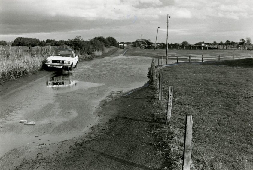 A car attempting to negotiate a large puddle of water on the Monifieth road to the rubbish dump next to Riverview Park in October 1984.