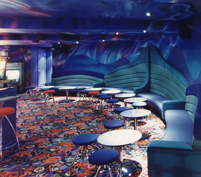Stools and booths and the colourful carpet in the seating area at Enigma. 