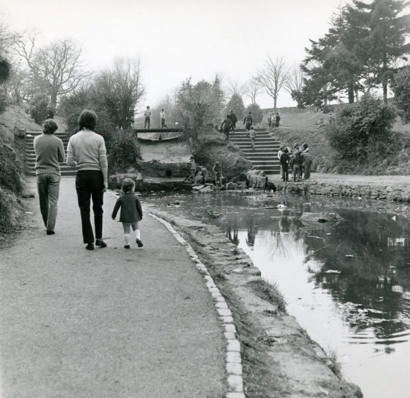 People walking beside the stream at Den O' Mains