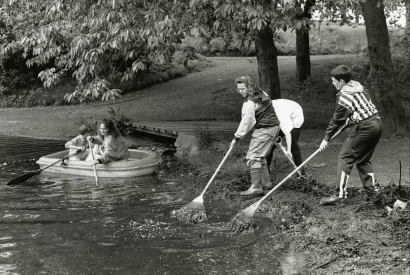 Pupils clean up the pond while two people boat in the background