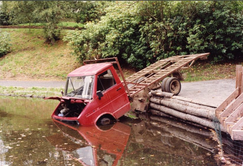 A partially submerged tow truck sits in the water at Den O' Mains