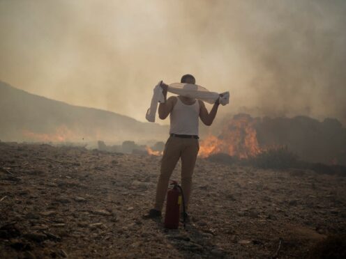 A man wraps his shirt over his face as he tries to extinguish a fire, near the seaside resort of Lindos, on the Aegean Sea island of Rhodes, southeastern Greece, on July 24 2023 (Petros Giannakouris/AP)
