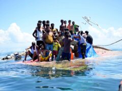 Rohingya refugees stand on their capsized boat as rescuers throw a rope to rescue them in the waters off West Aceh, Indonesia (Reza Saifullah/AP)