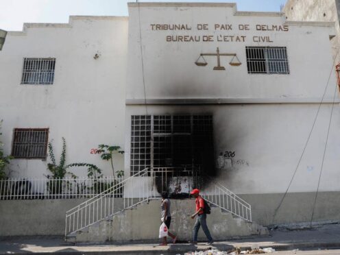 Pedestrians walk past a court building that was set on fire by gangs (Odelyn Joseph/AP)