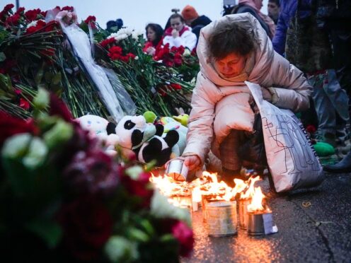 A woman lights candles at the fence next to the Crocus City Hall (Alexander Zemlianichenko/AP)