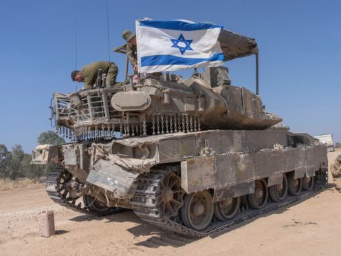 An Israeli soldier attaches an Israeli flag on top of an armoured personnel carrier in southern Israel (Ohad Zwigenberg/AP)