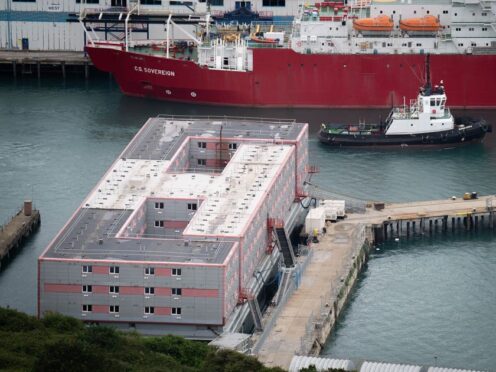 A tug boat passing the Bibby Stockholm accommodation barge at Portland Port in Dorset (PA)