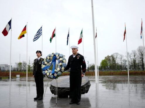 Two military personnel stand underneath the flags of Nato alliance members during a wreath-laying ceremony at Nato headquarters in Brussels (Virginia Mayo/AP)
