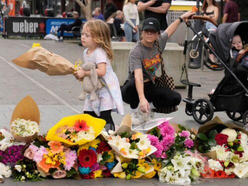 A young child carries flowers to place as a tribute near the scene at Bondi Junction in Sydney (Rick Rycroft/AP)
