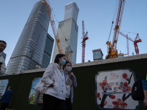Women wearing masks pass by construction cranes near the central business district in Beijing, Tuesday, April 16, 2024. China’s economy expanded at a faster than expected pace in the first three months of the year, helped by policies aimed at stimulating growth and stronger demand, the government said Tuesday. (AP Photo/Ng Han Guan)