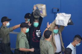 Pro-democracy activist Leung Kwok-hung, left, raises his hands as he is escorted to a prison van for a court hearing (AP)