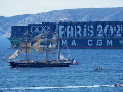 The Belem, the three-masted sailing ship bringing the Olympic flame from Greece, sails past a container ship decorated with the Paris 2024 logo when approaching Marseille, southern France (Laurent Cipriani/AP)