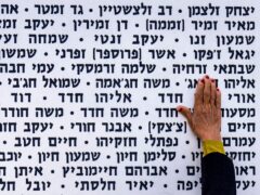 A woman touches the wall with names of fallen soldiers during Israel’s annual Memorial Day (Ariel Schalit/AP)