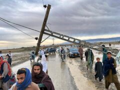 People pass by a damaged electric pole caused by flooding (AP Photo/Habib Ullah)