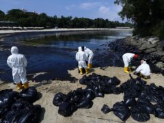 Workers clean an oil spill along Sentosa’s Tanjong Beach area in Singapore (Suhaimi Abdullah/AP)