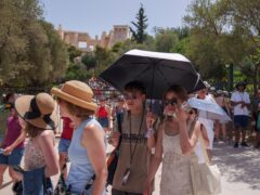 Tourists wearing hats or sheltering under umbrellas leave the Acropolis in Athens amid soaring temperatures (Petros Giannakouris/AP)