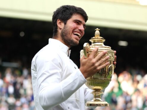 Carlos Alcaraz smiles while holding the Wimbledon trophy (Steven Paston/PA)