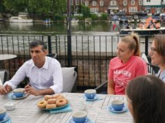 Rishi Sunak and the parliamentary candidate for Henley Caroline Newton (far right) speaking to rowing club members while Liberal Democrat supporters pass by on a boat, during a visit to the Leander Club in Henley-on-Thames, Oxfordshire (Jonathan Brady/PA)