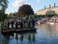 People sit on the banks of the River Cam and lawns of King’s College in Cambridge, as they listen to The King’s Men perform (Joe Giddens/PA)