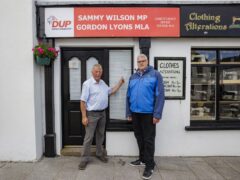 The DUP’s Sammy Wilson (left) and party leader Gavin Robinson stand beside the damage from four projectiles to the window and door of the offices of DUP parliamentary candidate Mr Wilson (Liam McBurney/PA)