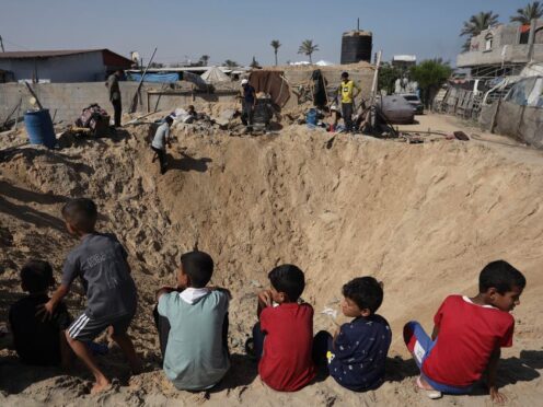 Palestinian children sit at the edge of a crater after an Israeli airstrike in Khan Younis, southern Gaza Strip, on Friday (Jehad Alshrafi/AP)