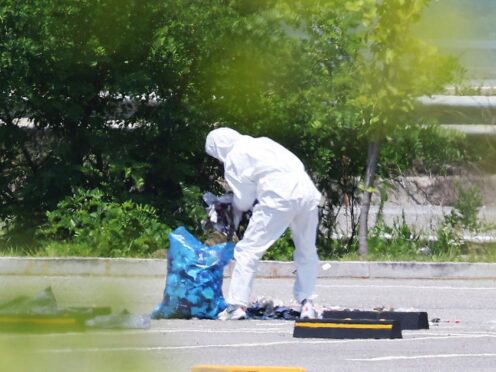 An officer wearing protective gear collects rubbish from a balloon presumably sent by North Korea, in Siheung, South Korea (Yonhap via AP)